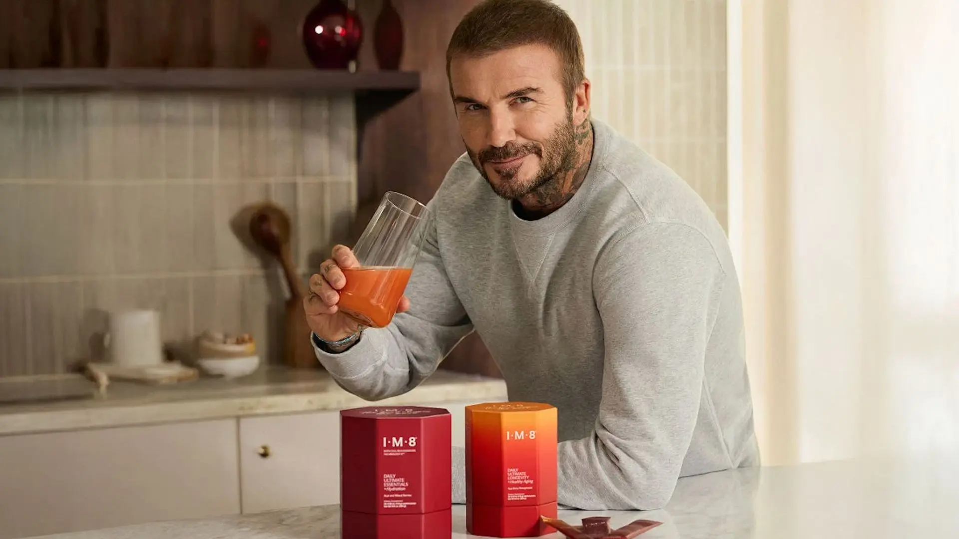 David Beckham holding an IM8 supplement drink with IM8 product boxes
